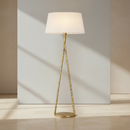 A modern floor lamp with a tapered white fabric shade and a textured gold metal base in a triangular design, shown against a plain white background.