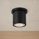 A modern black cylindrical ceiling light fixture with a textured glass shade, shown illuminated against a neutral beige textured background.