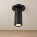 A modern matte black cylindrical ceiling light fixture shown mounted against a textured beige wall, illuminated from within.
