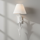 A white wall sconce with a tapered fabric shade and sculptural leaf-like metal arms, shown against a plain white background.