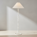 A white floor lamp with a sculptural, leafy branch-like metal base and a tapered off-white fabric shade, shown illuminated against a plain white background.