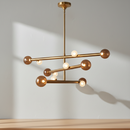 A modern chandelier with a brushed brass/gold finish, featuring multiple spherical bulbs on intersecting horizontal bars, suspended from a central rod against a plain white background.