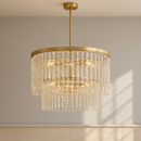 A gold-finished multi-tiered chandelier with cascading clear crystal prisms, shown hanging from a ceiling in an indoor room with paneled walls.