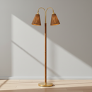 A modern two-light floor lamp with a polished brass or gold-finished metal frame, dual curved arms, and two tapered brown pleated fabric shades, set against a plain white background.