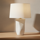 A modern table lamp with a textured off-white ceramic base and a matching fabric drum shade, shown illuminated against a plain white background.